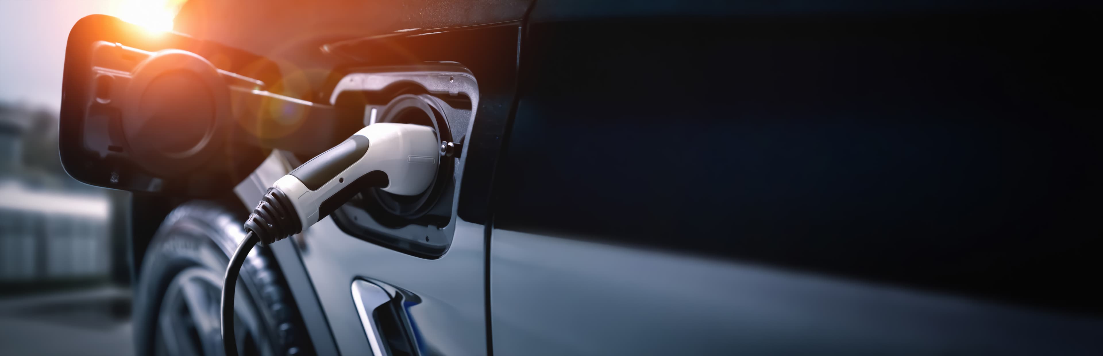 Charging connector plugged into an electric vehicle at sunset