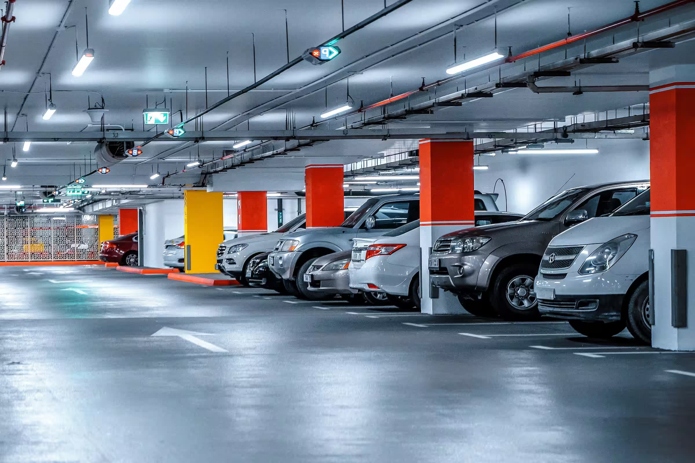 Underground residential parking garage with rows of parked cars and red accent columns