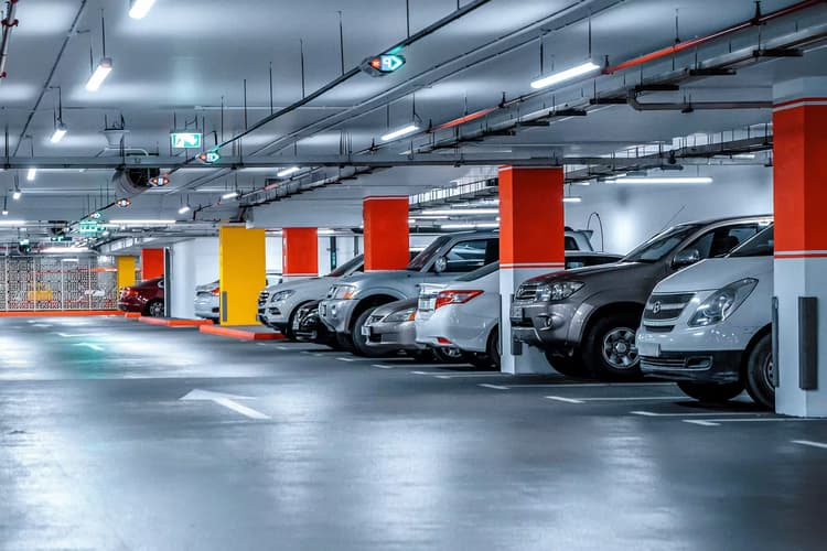 Underground residential parking garage with rows of parked cars and red accent columns