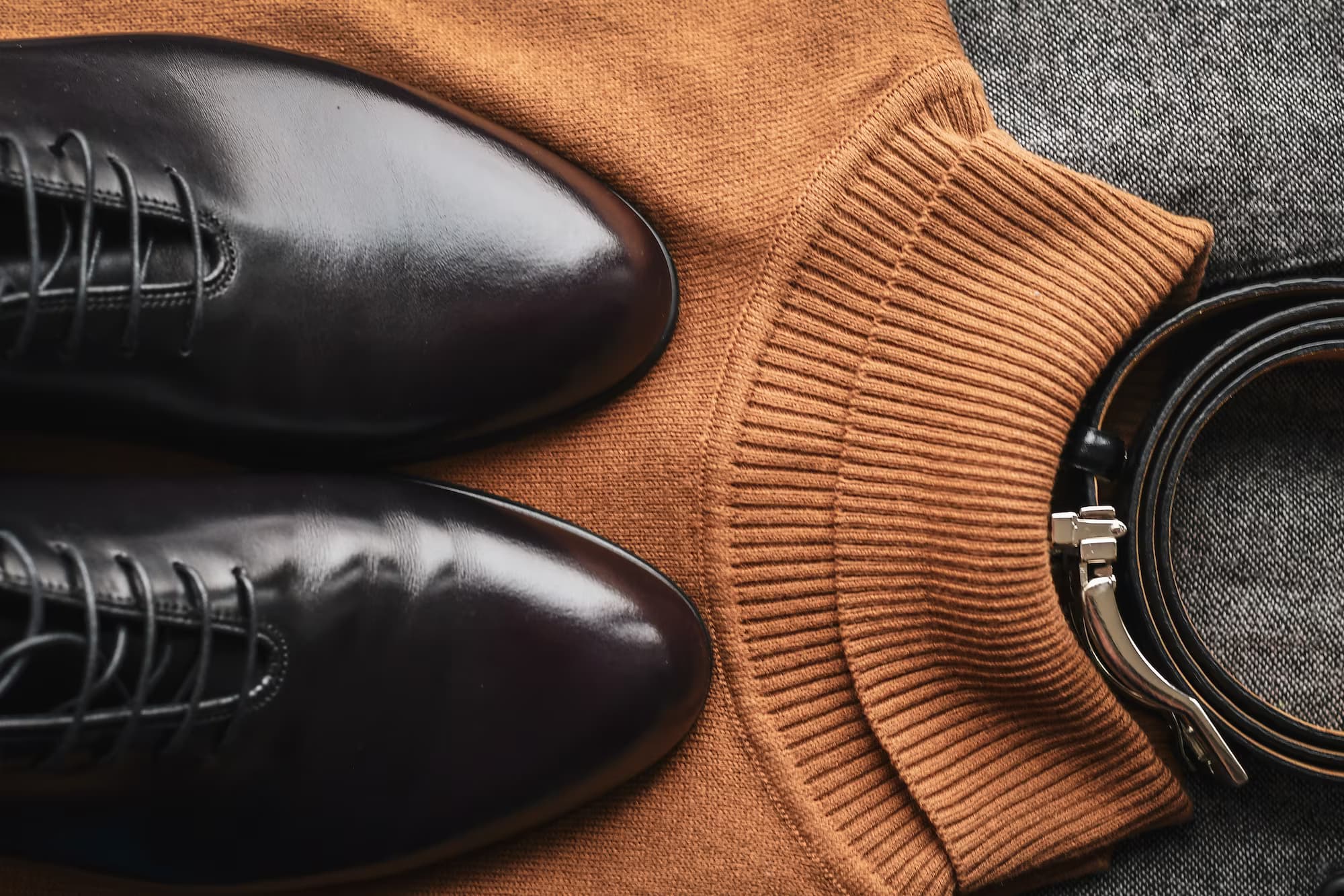 Flat lay of leather shoes, a folded knit sweater, and a belt