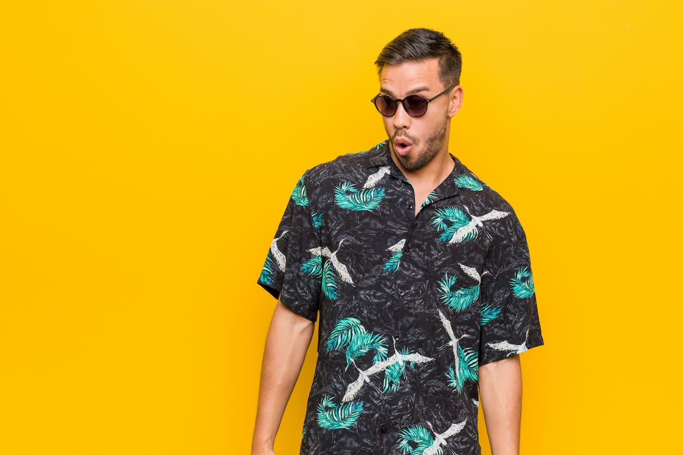 Model in a printed short-sleeve shirt and sunglasses against a yellow backdrop