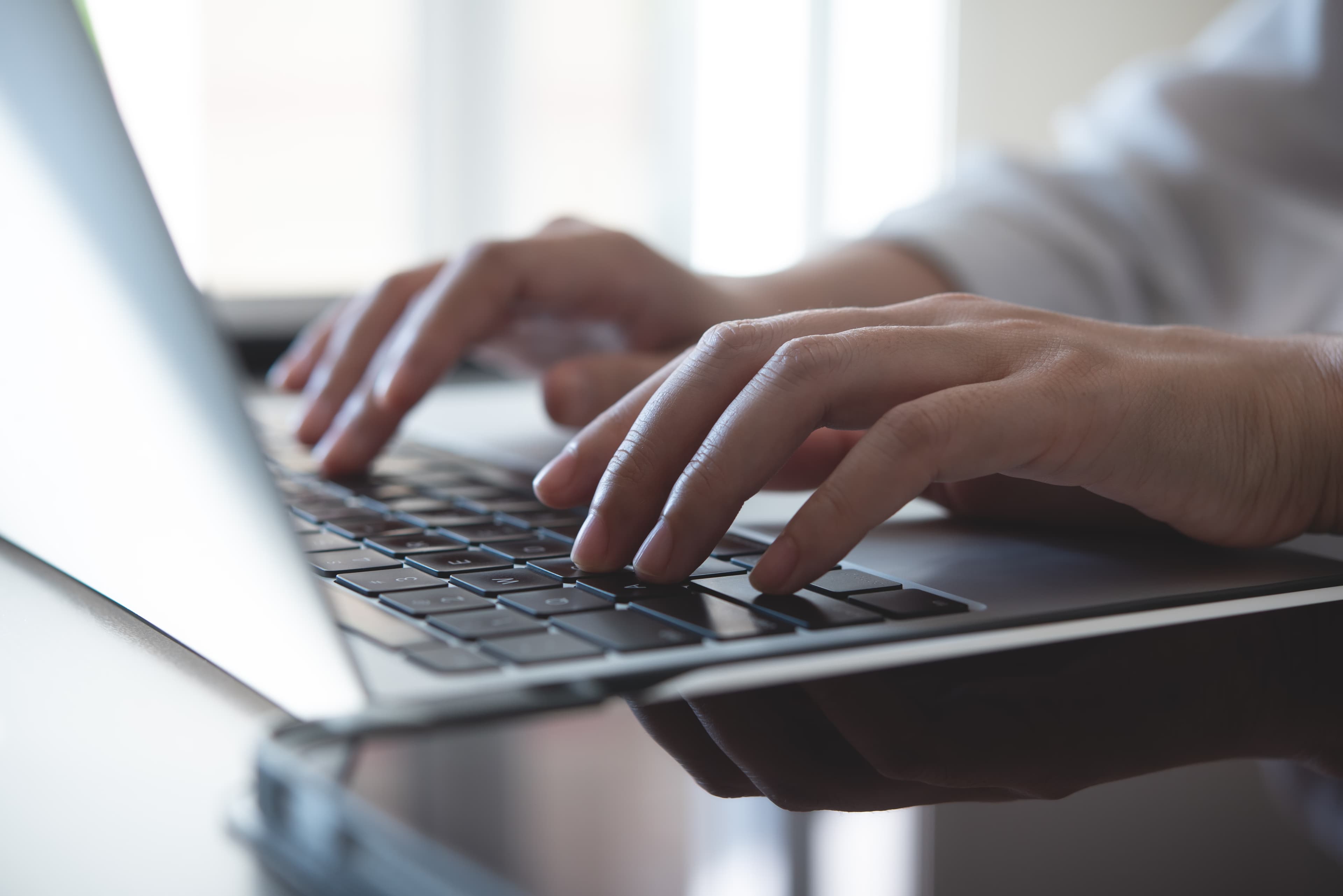 Hands typing on a laptop keyboard in a bright office