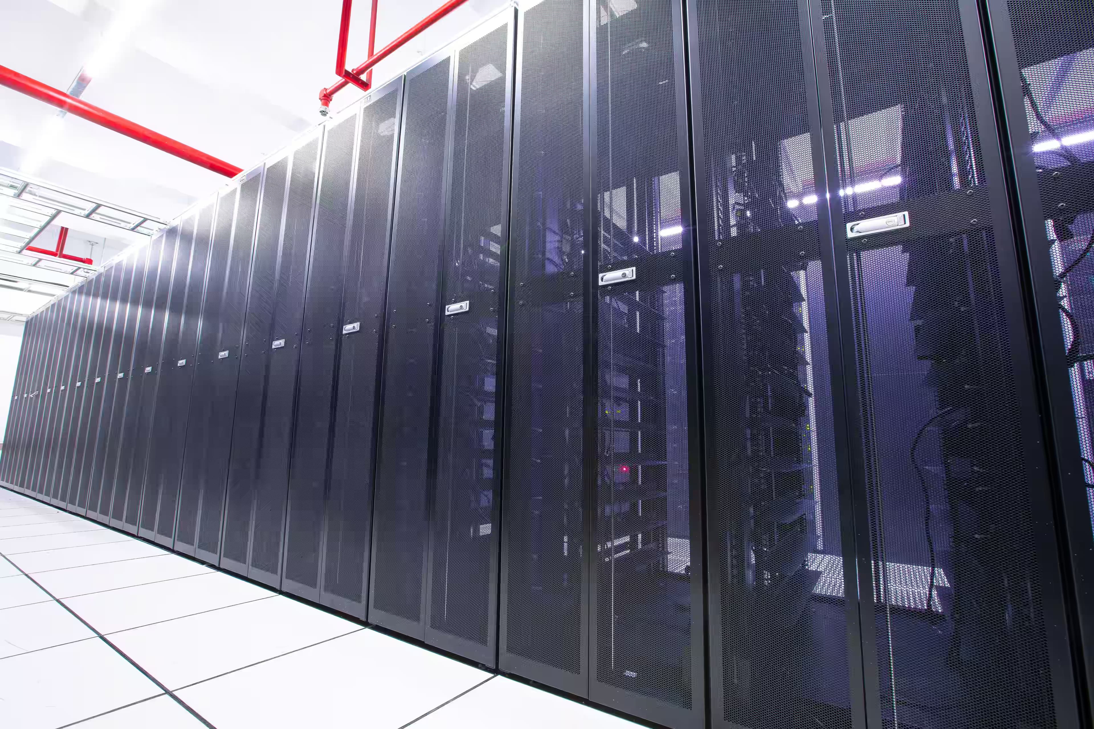 Row of server cabinets in a bright modern data centre with red overhead pipework