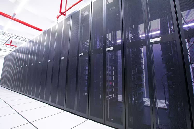 Row of server cabinets in a bright modern data centre with red overhead pipework