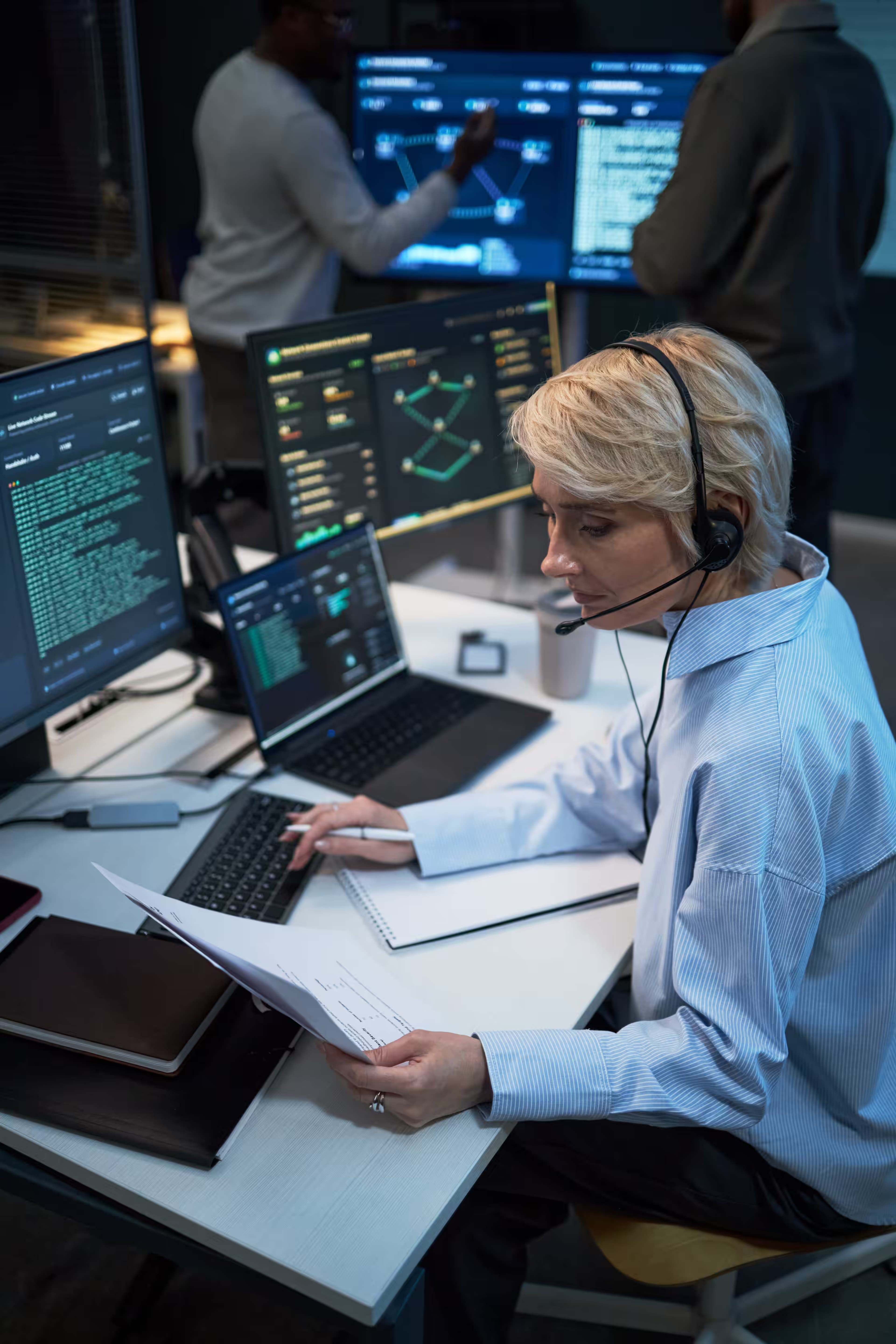 Network operations analyst reviewing printed documentation at a monitoring desk
