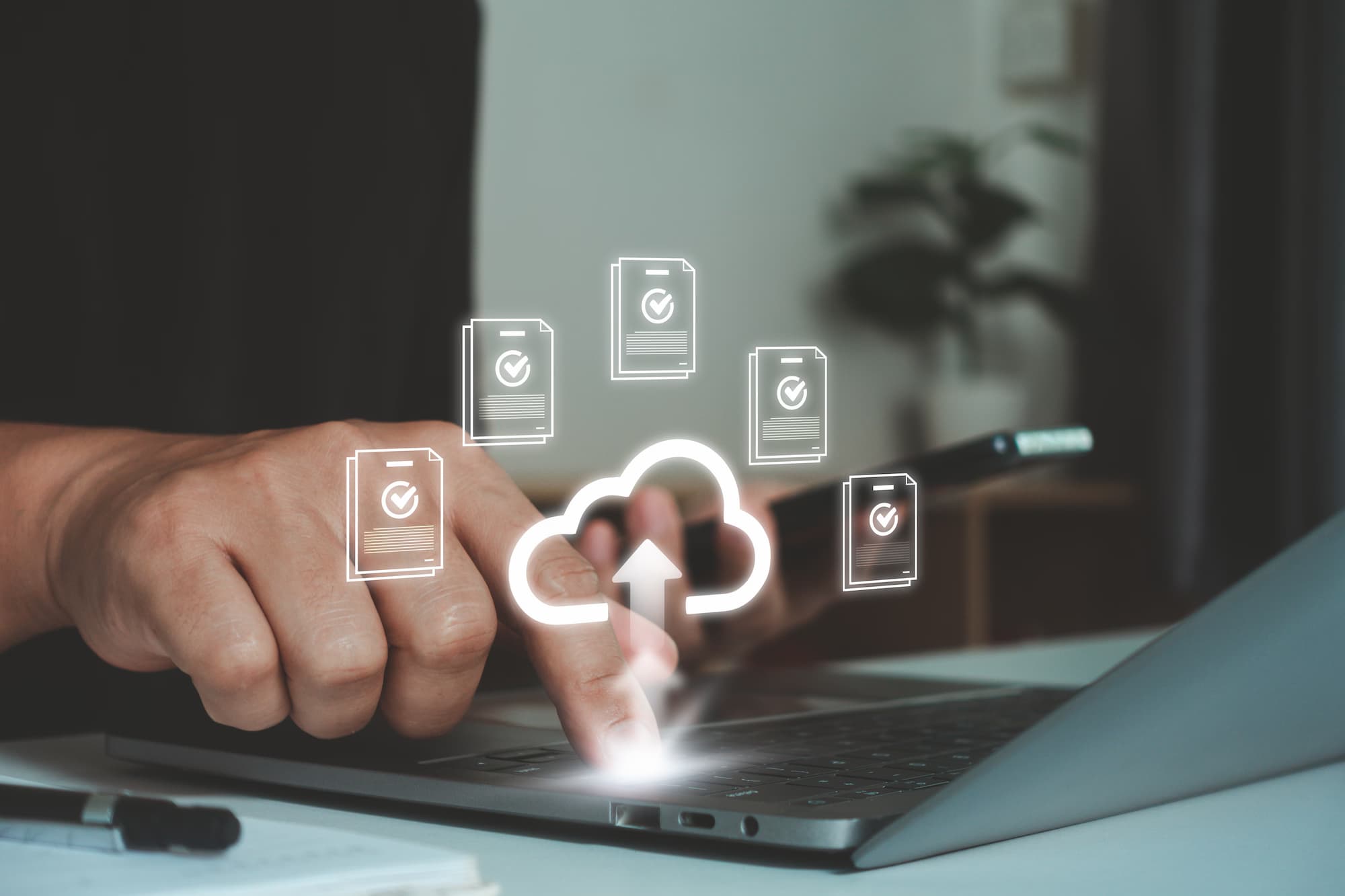 Hand at a laptop with validated files syncing up to a cloud icon